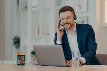 Fototapeta premium Young man in suit talking on webcam conference on laptop at home