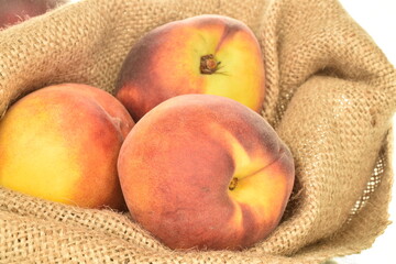 Several ripe organic peaches with a bag of jute, close-up, isolated on white.