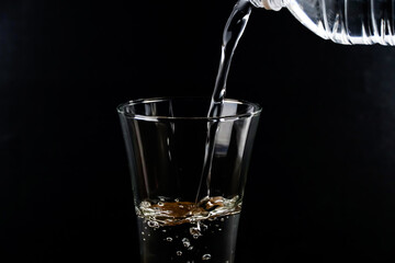 Pouring water into the glass on a black background.	