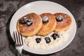 Healthy breakfast of cottage cheese pancakes, syrniki with blueberries and sour cream close-up in a plate on the table. Traditional Russian / Ukrainian cuisine, breakfast
