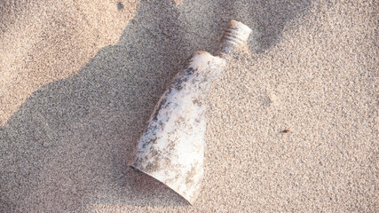 Bote de plástico de crema solar deteriorado semi enterrado por al arena de la playa
