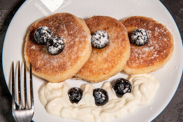 Healthy breakfast of cottage cheese pancakes, syrniki with blueberries and sour cream close-up in a plate on the table. Traditional Russian / Ukrainian cuisine, breakfast