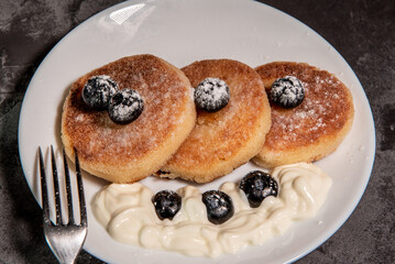 Healthy breakfast of cottage cheese pancakes, syrniki with blueberries and sour cream close-up in a plate on the table. Traditional Russian / Ukrainian cuisine, breakfast