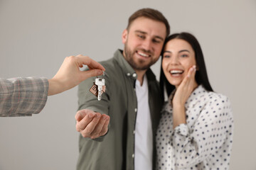Real estate agent giving key to happy young couple against grey background, focus on hands