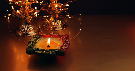 Closeup of a candlestick with burning candle next to ornaments wrapped in light garland