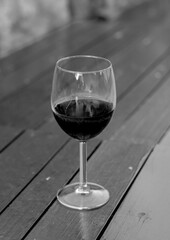 Glass of red wine on the wooden table.  Black and white. Selective focus.