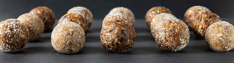 Homemade energy balls on a dark background close up. Banner. Candy with dried apricots, raisins, dates, prunes, walnuts and coconut.