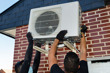 Técnicos del aire acondicionado colocando máquina compresora en fachada de chalet.