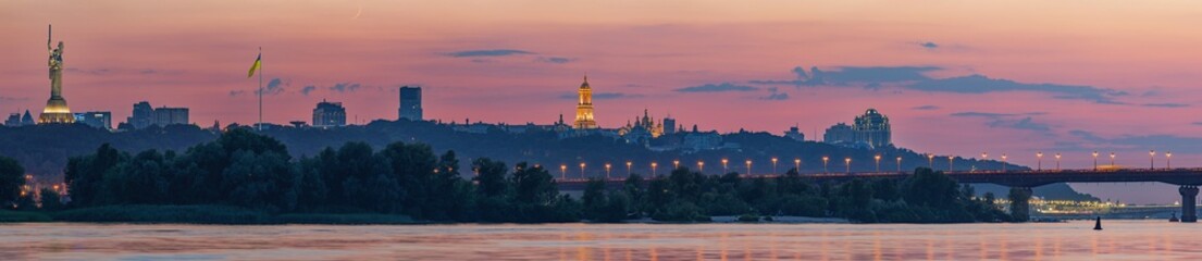 Uitzicht op de Kiev-Pechersk Lavra, de bruggen van Kiev en de rivier de Dnjepr, na zonsondergang wordt een dunne halve maan aan de roze lucht gezien.