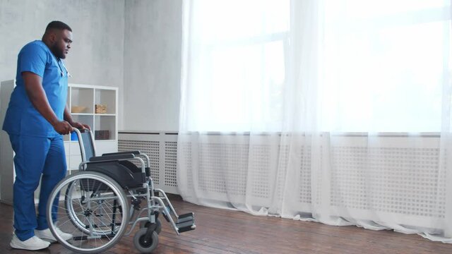 African-American caregiver and an empty wheelchair. Professional nurse in a nursing home. Assistance, rehabilitation and health care.