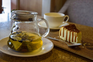 Glass teapot with green tea, mint and lemon, cup of tea, small teaspoon and half-eaten piece of...
