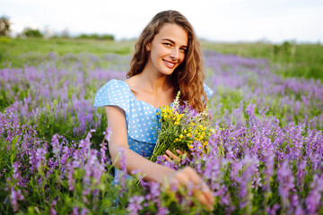 Fototapeta na wymiar Young woman in stylish summer dress feeling free in the field with flowers in sunshine. Nature, vacation, relax and lifestyle. Summer landscape.