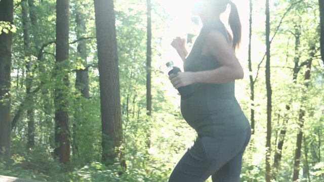 Active pregnant woman running in summer park or forest. Expectant mother exercising healthy lifestyle jogging workout outside. Pregnancy sport and fitness training concept.