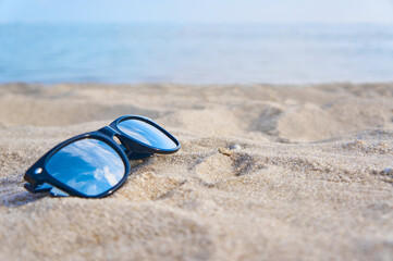 Fototapeta na wymiar Mirror sunglasses on the sand beach with blue sky reflection