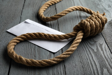 Rope noose and blank envelope on grey wooden table, closeup