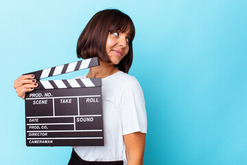 Young mixed race woman holding a clapper board looks aside smiling, cheerful and pleasant.