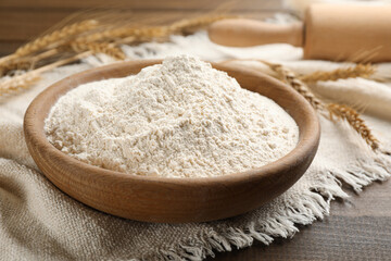 Fototapeta na wymiar Bowl with wheat flour on wooden table, closeup