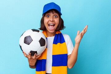 Young mixed race woman watching soccer isolated on blue background receiving a pleasant surprise, excited and raising hands.