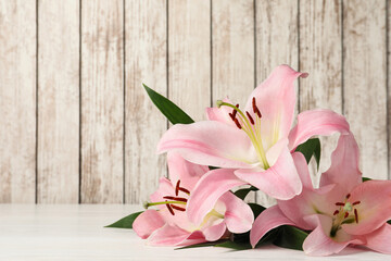 Beautiful pink lily flowers on white wooden table, space for text
