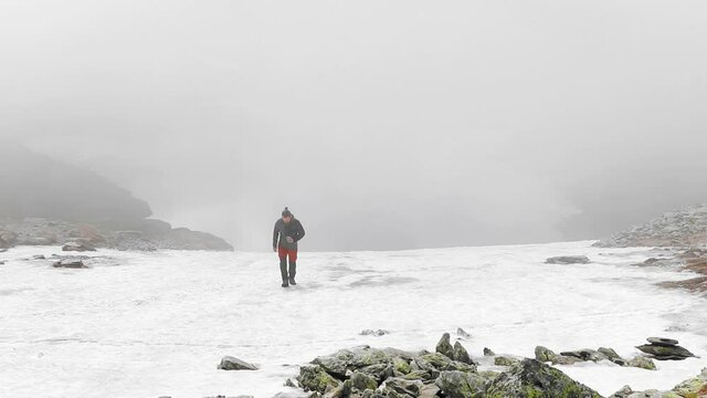 A hiker sits and admires a beautiful glacier lake with snow and fog