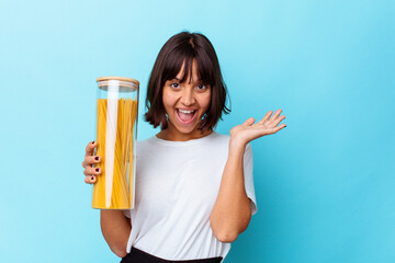 Young mixed race woman holding pasta jar isolated on blue background showing a copy space on a palm and holding another hand on waist.