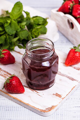 Jar of strawberry jam on wooden rustic board.