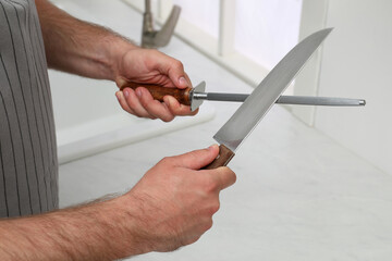Man sharpening knife in kitchen, closeup view