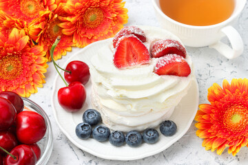 mini meringue with whipped cream cake decorated with fresh fruits with gerbera flowers and cup of tea at the background
