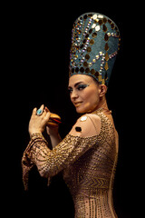 Portrait of young woman in image of Nefertiti in art performance isolated on dark background. Retro style, comparison of eras, humor concept.