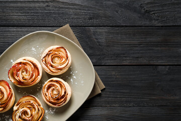 Fototapeta premium Freshly baked apple roses on dark wooden table, top view. Space for text