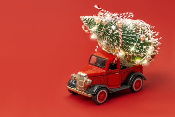 Red small retro toy truck with sparkling Christmas tree lights on truck body on red background. Delivery, christmas, New Year concept. Copy space, selective focus.