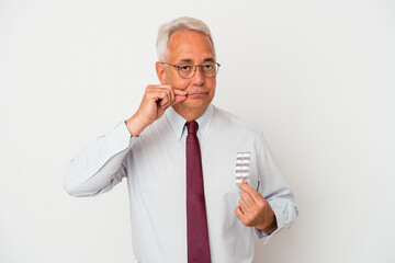 Senior american man holding pills isolated on white background with fingers on lips keeping a secret.