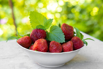 Strawberry with lemon mint leaves in white plate on green background