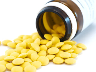 Round yellow pills with brown glass phial on white background