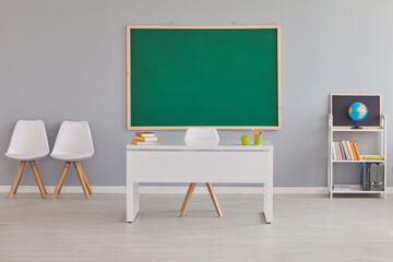 Interior of a modern light empty school classroom with a clean green blackboard, teacher's desk,...