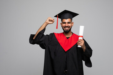 education, graduation and people concept - happy smiling indian male graduate student in mortar board and bachelor gown with diploma over grey background