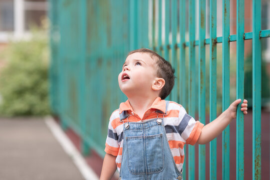 A boy on the playground, a tall green fence, a fencing, with peeling paint.