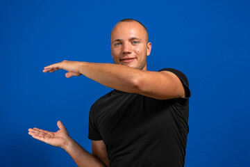 Naklejka premium Young man with black shirt over isolated blue background holding copyspace imaginary on the palm to insert an ad. Imagination concept