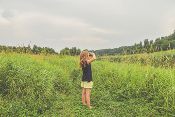 Naklejka na ściany i meble a child girl stands in a meadow and looks through binoculars