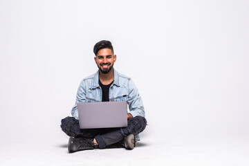 Handsome guy working on a laptop and sitting on a floor, isolated against white background