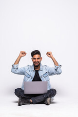 Happy man sitting on the floor with a laptop over a white background