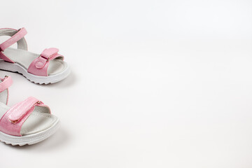 Fototapeta na wymiar Pink children's sandals made of shiny leather with Velcro fasteners, flat white soles, isolated on a white background. A pair of fashionable children's sandals for a comfortable walk. 