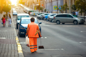 Woman in orange uniform with broomstick and scoop for garbage sweep city street. Municipal worker clean up street in the evening. worker in orange uniform collecting garbage from road and sidewalk