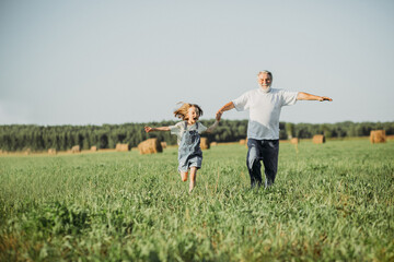 The girl sits on the shoulders of her grandfather while walking in the field. Happy vacation concept with grandparent