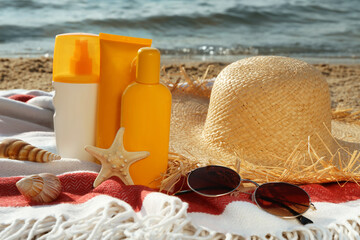 Fototapeta na wymiar Sun protection products and beach accessories on blanket near sea
