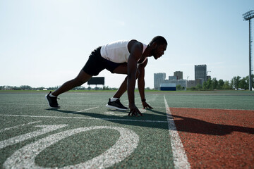 Photo from the side. African american athlete run preparing for the race while standing in a pose...