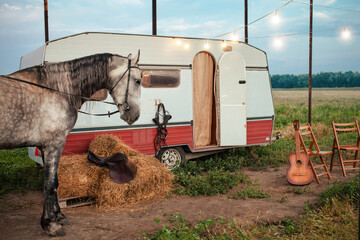 gray horse, mobile trailer, glowing garland, guitar, folding chairs for rest, bales of hay, saddle...