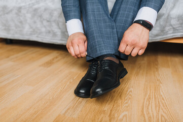 A man, a businessman, ties his shoelaces with his hands on black shiny leather shoes, getting ready...