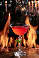 red cocktail in a beautiful glass on copper designer bar counter, the background of real fire. High quality photo