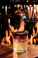 yellow and red wine cocktail in a beautiful tumbler, rocks glass on copper designer bar counter, the background of real fire. High quality photo